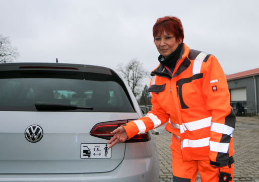 Bauhof-Vorarbeiterin Sabine Saboth präsentiert den neuen Aufkleber für mehr Verkehrssicherheit.