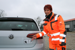 Bauhof-Vorarbeiterin Sabine Saboth präsentiert den neuen Aufkleber für mehr Verkehrssicherheit.